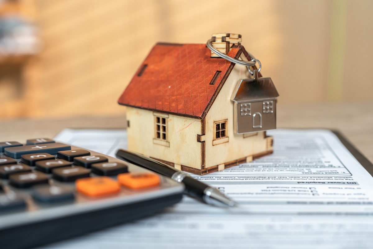 Small wooden model home beside a pen and calculator on a desk