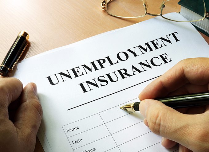 A person fills out an unemployment insurance form on a desk, with glasses and a pen visible nearby.